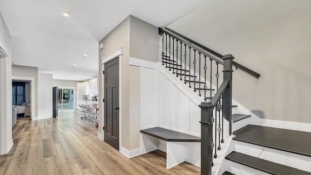 A modern interior with a wooden floor, a staircase with black balusters, and a view into a dining area. - 6 BR, 4BA Franklin, IN Home (Franklin)