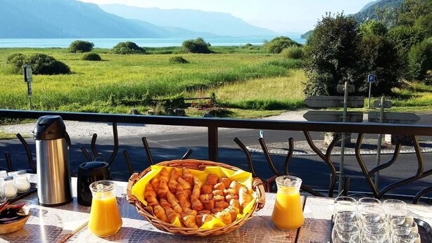 A table with croissants, juice, and a view of a lake and mountains. - Auberge de Portout (Chanaz)