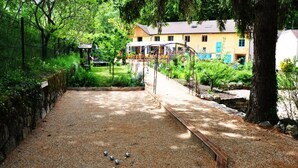 A courtyard with a shuffleboard table, surrounded by greenery and a building in the background. - Auberge de Portout (Chanaz)