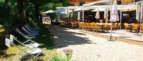 Un espace extérieur aménagé avec des tables et des chaises, une terrasse couverte et un bâtiment doté d’un toit en pente.