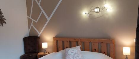 A bedroom with a wooden bed, two bedside tables, a wall-mounted light fixture, and a decorative wall panel.