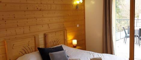 A wooden bed with pillows and a bedside lamp in a room with wooden walls and a view of the outdoors.