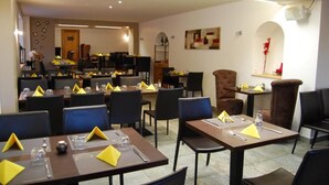 A dining area with multiple tables and chairs, some with yellow napkins. There are decorative items on the walls and a door in the background. - Auberge de Portout (Chanaz)