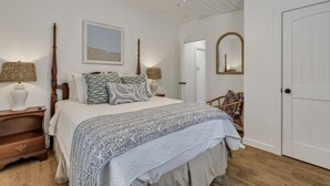 Una camera da letto con un letto grande, due comodini, una ventola a soffitto, un quadro incorniciato, uno specchio e una porta.