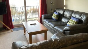 Ein Wohnzimmer mit einer Ledersofa, einem Holztisch und Blick auf einen See durch eine Schiebetür.