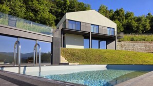 A modern house with a swimming pool, large windows, and a grassy hill in the background. - Casa do Barbeiro | Pool | River Minho Views | Agro-tourism (Melgaço)