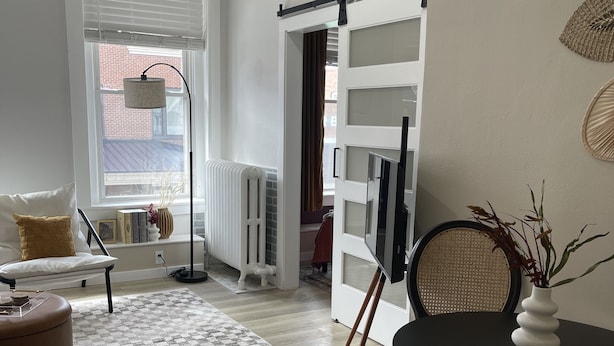 A modern living room with a sofa, a round table with a vase, a patterned rug, and a view of the outside through a window. - Squareview Stays - Modern Apartment On the Square (Indianola)