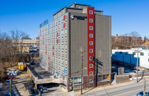 A multi-story hotel with a distinctive red and grey facade, a parking lot, and a clear sky.
