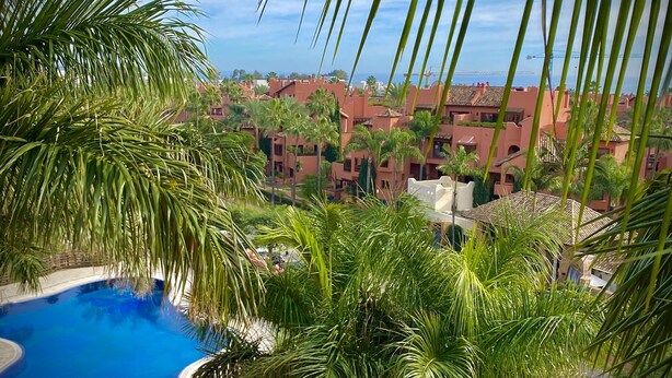 A pool surrounded by palm trees and a view of a residential area with red buildings. - Luxury and spacious 3-bed Penthouse apartment in fabulous Gualdalmansa (Gualdalmansa)