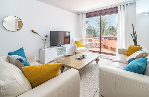 Relax in this stylish living room with a flat-screen TV, comfortable sofas, and a balcony offering views of palm trees.