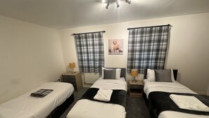 Een kamer met drie eenpersoonsbedden, elk met een nachtkastje en lamp, en een poster aan de muur.