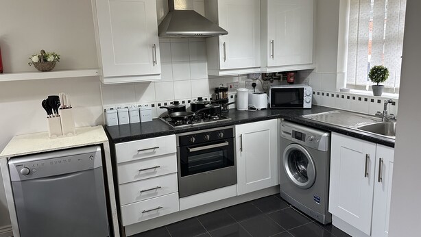 Een moderne keuken met witte kasten, een vaatwasser, een wasmachine, een fornuis, een magnetron en een spoelbak.