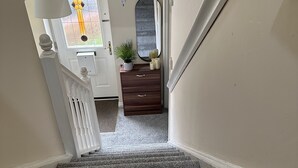 Een trap die leidt naar een kamer met een witte deur, een spiegel, een plant en een dressoir.