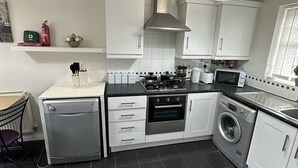 Een moderne keuken met witte kasten, een vaatwasser, een fornuis, een magnetron en een wasmachine.