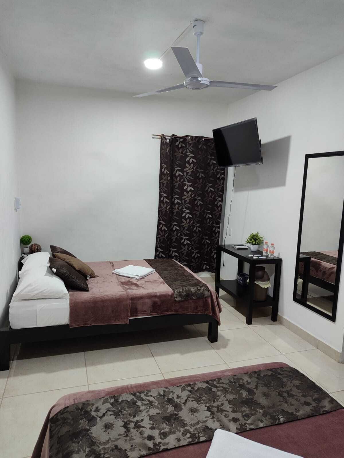 A bedroom with a bed, a desk, a TV, and a ceiling fan.