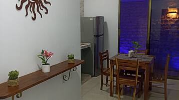 Un comedor con una mesa y sillas de madera, un refrigerador, una planta en maceta y un adorno en la pared.