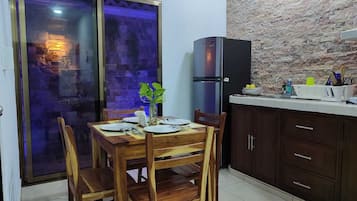 A dining area with a wooden table and chairs, a refrigerator, and a kitchen counter with cabinets.