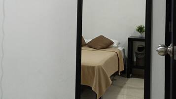A room with a bed, a bedside table, a small potted plant, and a flat-screen TV mounted on the wall.
