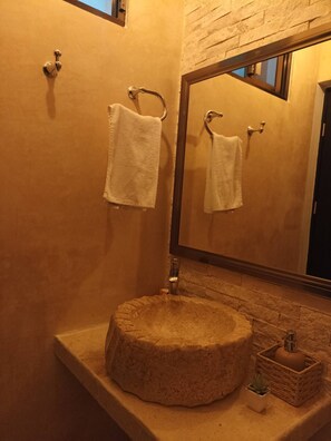 A bathroom with a round sink, two towels hanging on towel rings, a mirror, and a small potted plant on the counter. - Departamentos Chan Kiin (Valladolid)