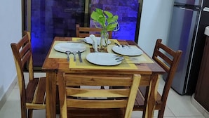 A dining area with a wooden table set for four, surrounded by chairs, a small plant, and a refrigerator in the background. - Departamentos Chan Kiin (Valladolid)