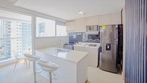 Una cocina moderna con un amplio ventanal, encimeras blancas y electrodomésticos de acero inoxidable.