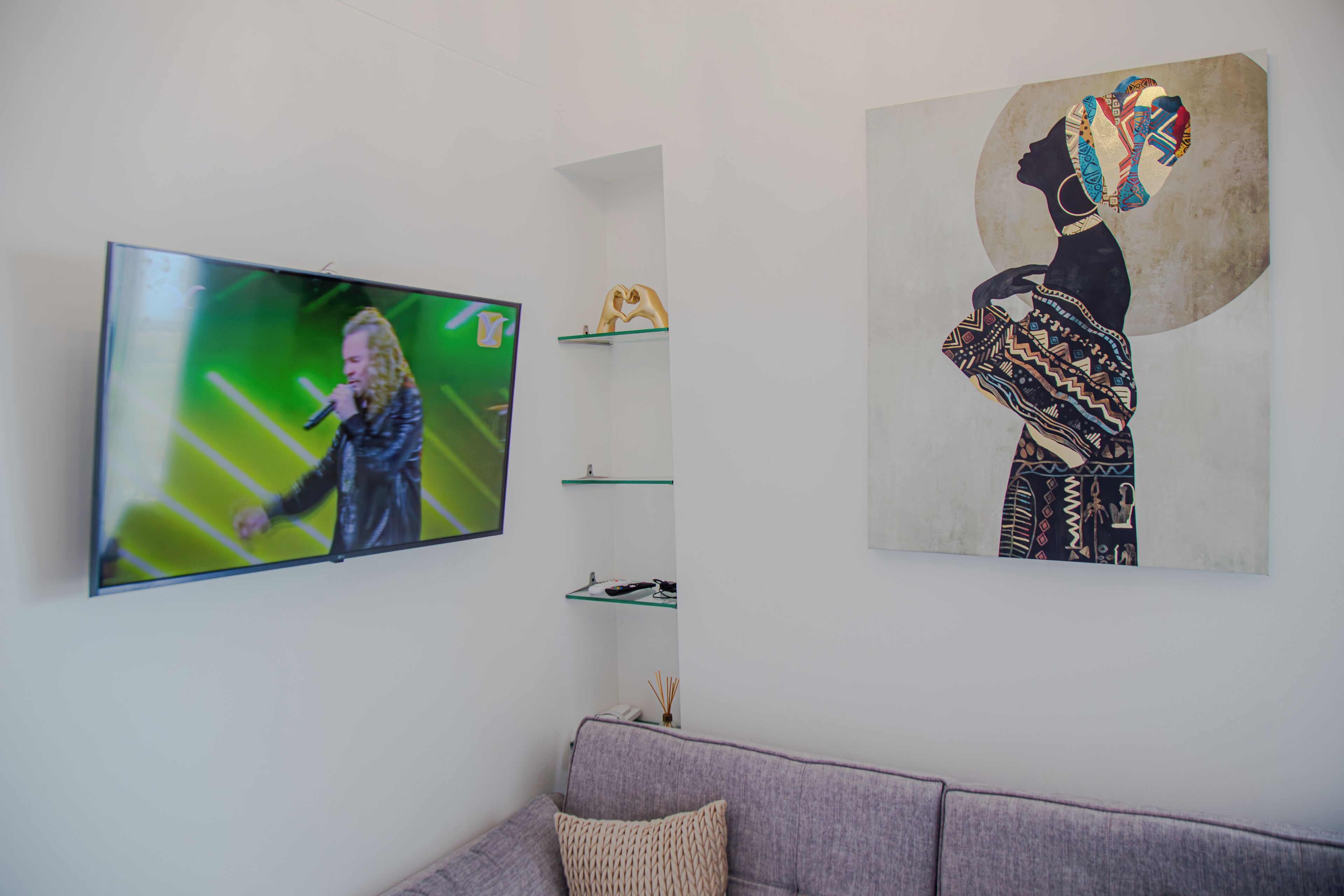 Ett vardagsrum med en platt-TV, en grå soffa och ett inramat konstverk på väggen.