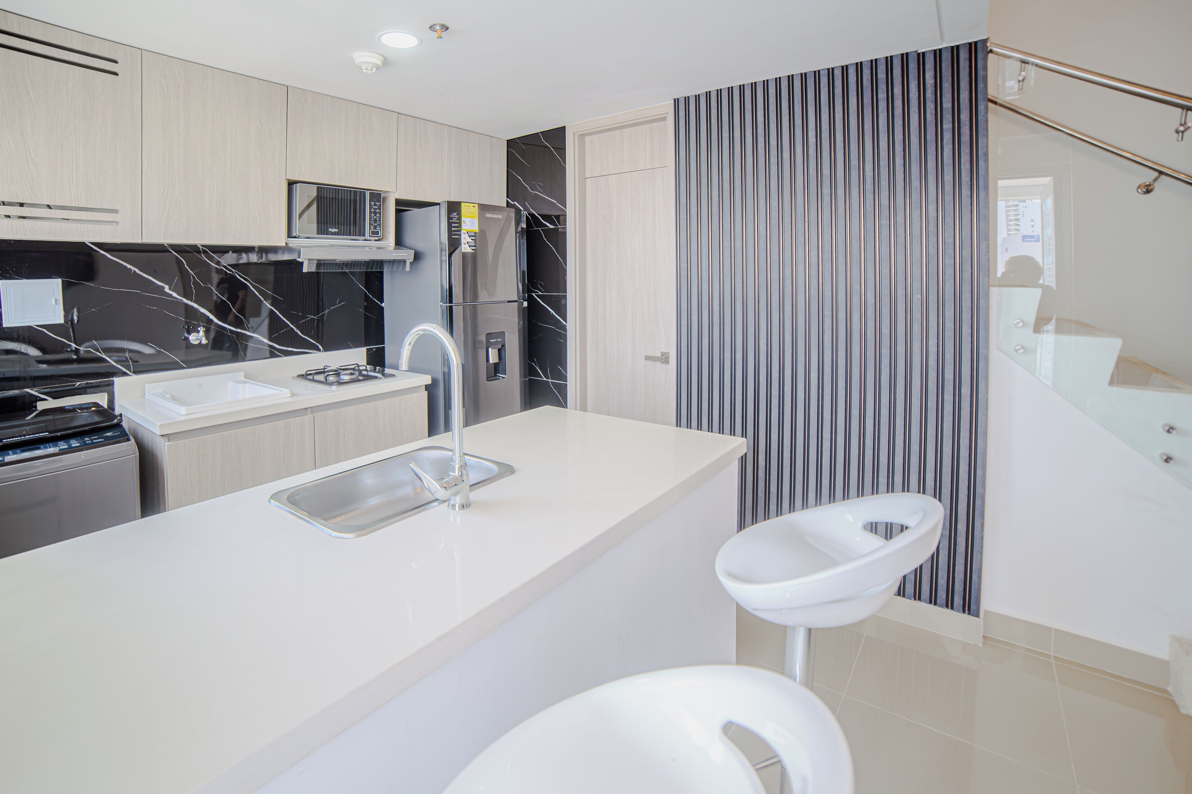 Een moderne keuken met een centraal eiland, roestvrijstalen apparatuur en een accentmuur met strepen.