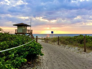 A beach path leading to a lifeguard tower with a view of the ocean at sunset.