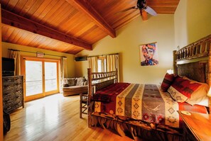 Une pièce avec un plafond en bois, un lit recouvert d’une couvre-lit à motifs, une chaise, une fenêtre avec des rideaux et un panneau indiquant la sortie.