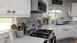 A modern kitchen with white cabinets, a stainless steel stove, and a window with a view of greenery. - PENION HOME! HOT TUB FOR 6/7 - SPACIOUS YARD FOR KIDS! (Austin)