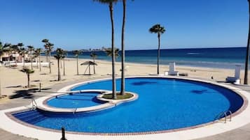 A swimming pool with a curved edge, surrounded by palm trees and a beach in the background.