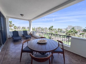A balcony with a round wooden table, two chairs, and a bowl of fruit.