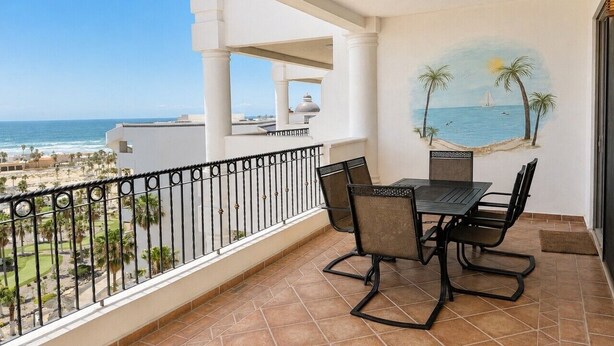 Un balcon avec une table et des chaises, offrant une vue sur la plage et l’océan.