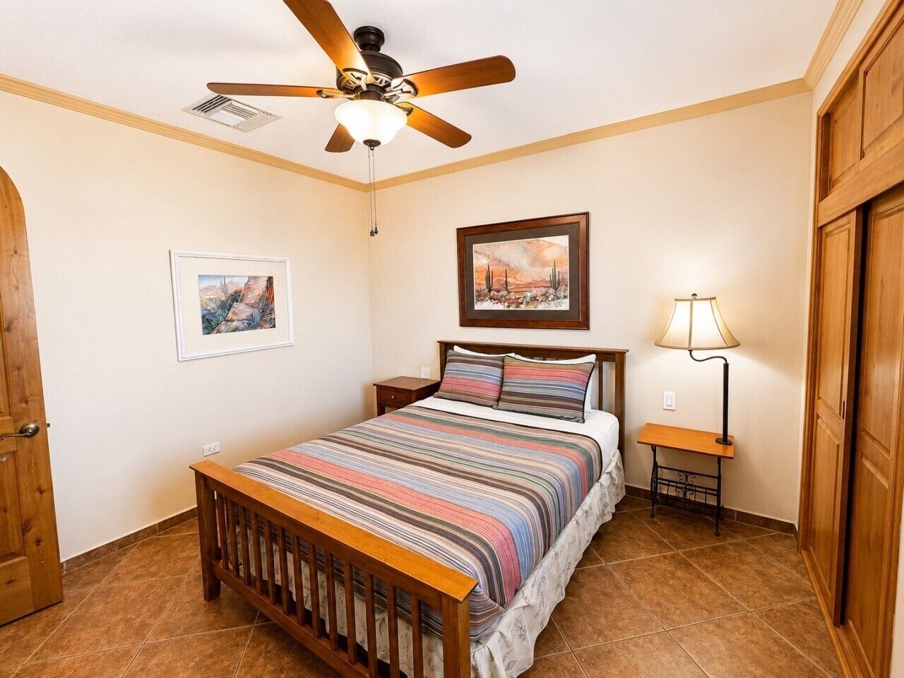 A bedroom with a bed, a ceiling fan, a nightstand, a lamp, and a door.