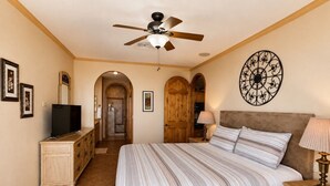 Une chambre à coucher comprenant un lit, un ventilateur de plafond, une télévision, une commode et un élément décoratif mural.