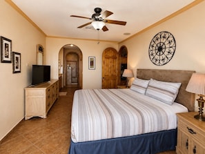 A bedroom with a bed, a ceiling fan, a TV, a dresser, and a decorative wall piece. - Casa Blanca D703 Pet Friendly Ocean View Condo (Puerto Peñasco)