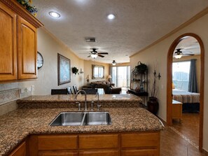 A kitchen with granite countertops, a double sink, wooden cabinets, and a ceiling fan.