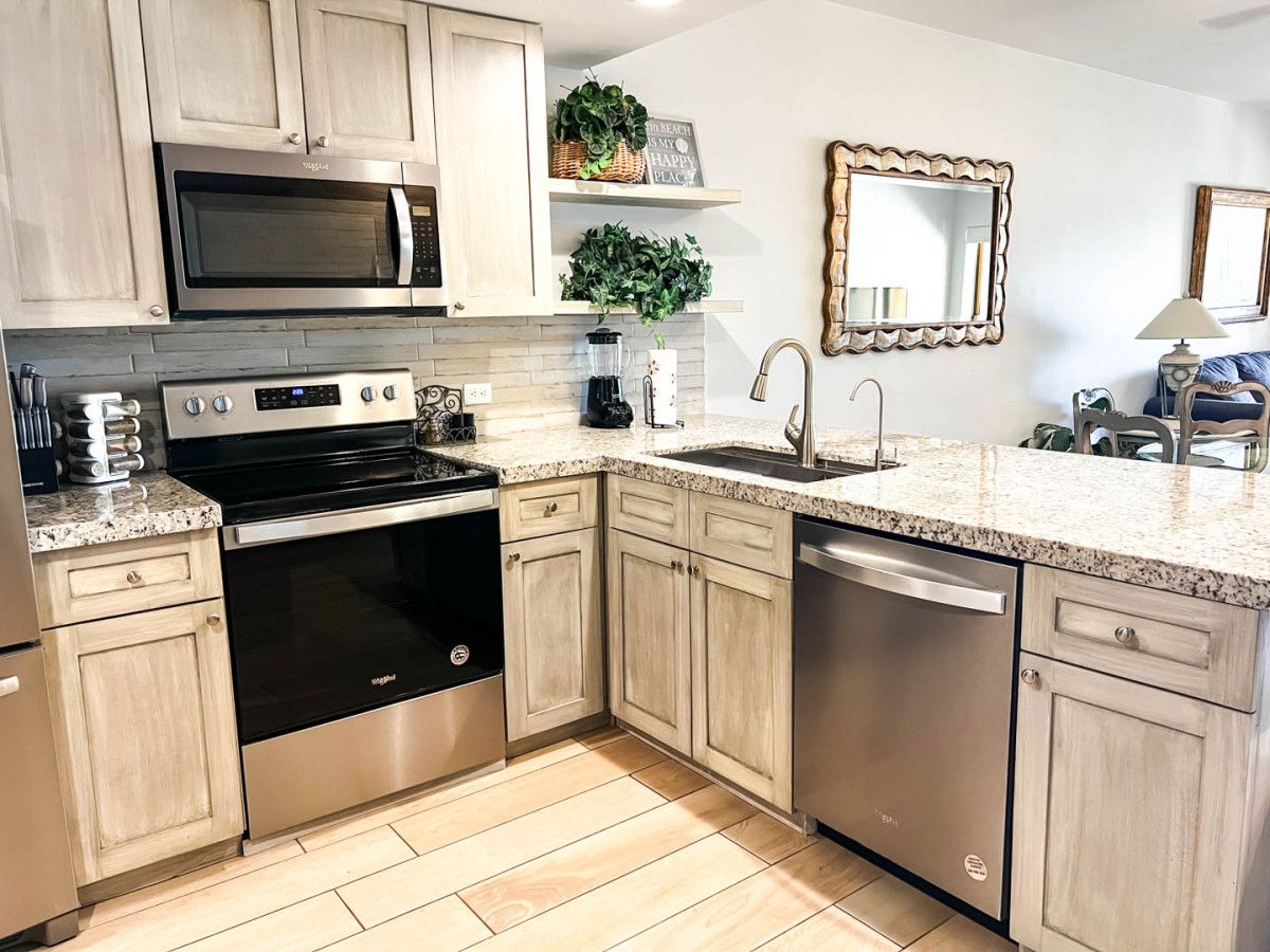 A modern kitchen with stainless steel appliances, light wood cabinetry, and a granite countertop.