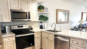 A modern kitchen with stainless steel appliances, light wood cabinets, a granite countertop, and a built-in microwave.