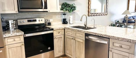 A modern kitchen with stainless steel appliances, light wood cabinetry, and a granite countertop.
