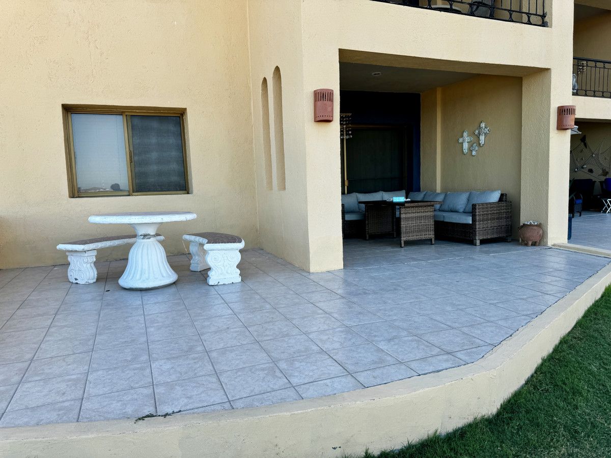 Um pátio com mesa, cadeiras, uma janela e a entrada de um edifício.