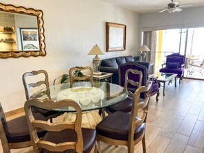 A dining area with a glass table surrounded by wooden chairs, a sofa, and a purple armchair in a well-lit room with a ceiling fan. - Princesa A101 Fresh Remodel, Directly on the Beach (Puerto Peñasco)
