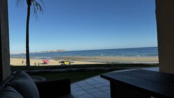 A patio with a view of a beach, a palm tree, and a distant shoreline.