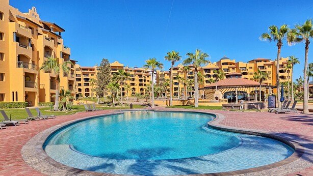 A swimming pool surrounded by palm trees and a building with balconies.