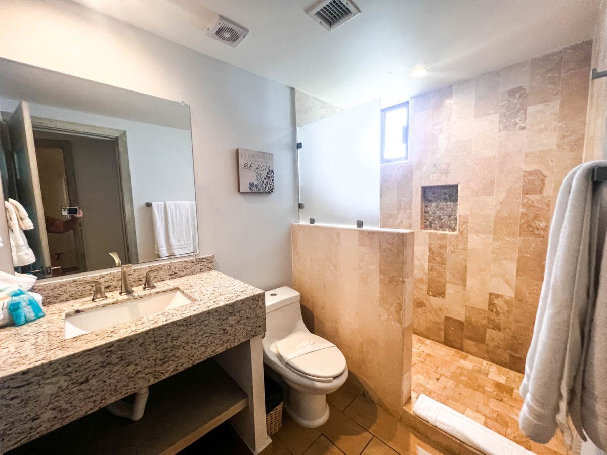Une salle de bain avec un lavabo sur un plan de travail en granit, des toilettes et une douche aux carreaux en pierre.