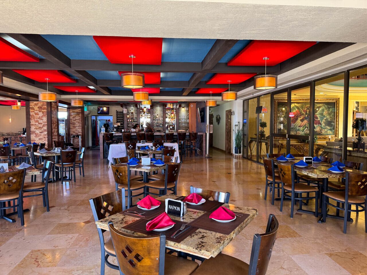 A spacious restaurant with multiple dining areas, a bar, and a view of the cityscape.