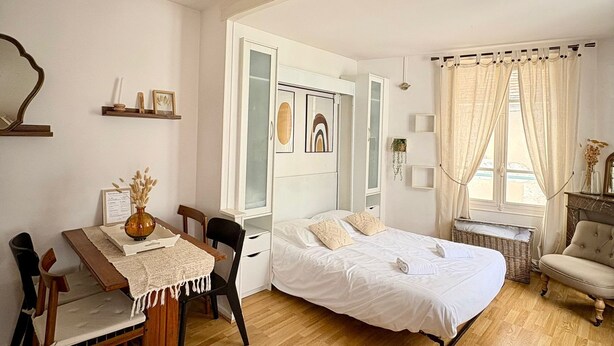 A room with a bed, a desk, chairs, a ceiling fan, and a window with curtains.