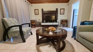 A living room with a round glass coffee table, a sofa, a patterned armchair, a television, and a fireplace. - Private Pool & Garden - Tranquil Retreat (Paradise Island)