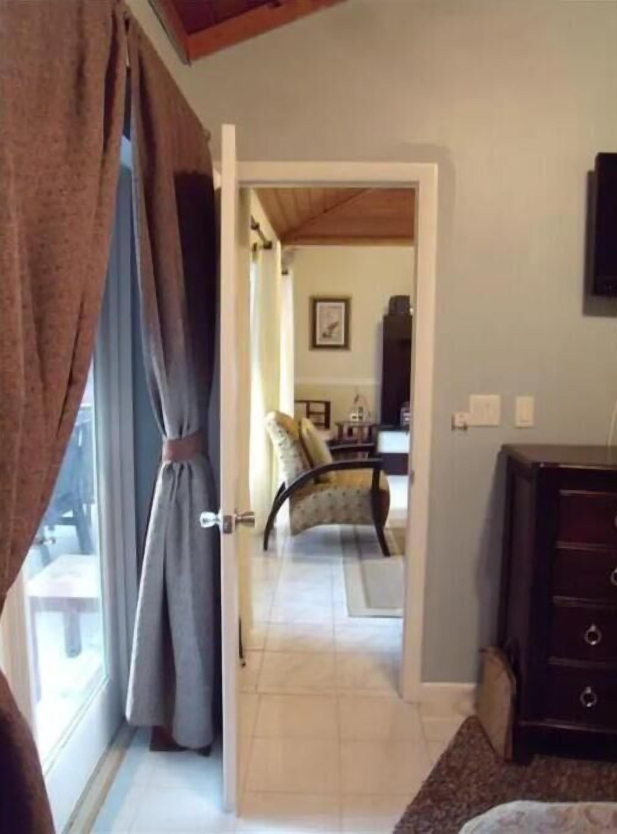 Um quarto com cama, cadeira, cômoda e janela com cortinas.