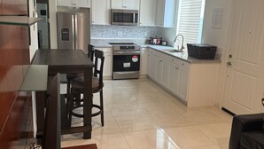 Una cocina moderna con armarios blancos, electrodomésticos de acero inoxidable y un comedor con televisor y control remoto.